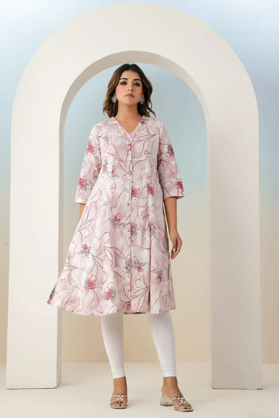 Woman wearing a pink floral dress standing in front of a white archway.